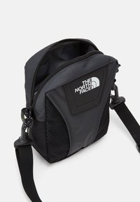 Sort nylon skuldertaske med mesh-detaljer, lynlåslukning og logo-patch. Har en justerbar rem og et kompakt rektangulært design.