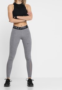 Black sports bra with cutout details; gray fitted leggings with a ribbed texture and black waistband featuring "NIKE PRO" logo, paired with black sneakers.
