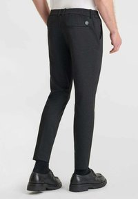 Zwarte op maat gemaakte broek met een slim fit, gestructureerde stof, riemlussen en een knoopzak op de rug, gecombineerd met zwarte leren schoenen.