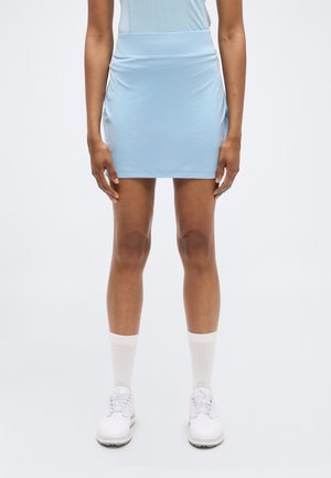 Lyseblå miniskjørt laget av mykt, elastisk stoff. Har høy midje og diskret rynking på sidene. Matchet med hvite sko og sokker.