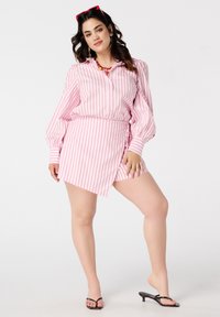 Chemise rayée rose à manches bouffantes longues, associée à une jupe asymétrique assortie. Présente un col et une texture de tissu lisse.