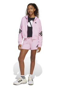 Sudadera corta rosa con rayas negras en las mangas, camiseta gráfica negra, pantalones cortos rosa y zapatillas blancas con acentos negros y calcetines a rayas.