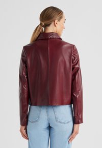 Burgunderfarbene Lederjacke in cropped Form mit kragenförmigem Ausschnitt und langen Ärmeln, die eine glatte Textur und ein schlichtes Design aufweist.