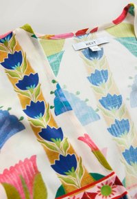 Light fabric with vibrant floral patterns in blue, pink, green, and mustard, featuring a "NEXT" brand label at the collar.