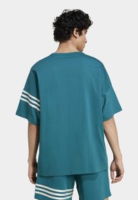 Teal värvi ülim suur t-särk, mis on valmistatud puuvillast, millel on ümmargune kaelus, lühikesed varrukad ja valged triibud varrukatel. Ükslane tagapoolt vaade.