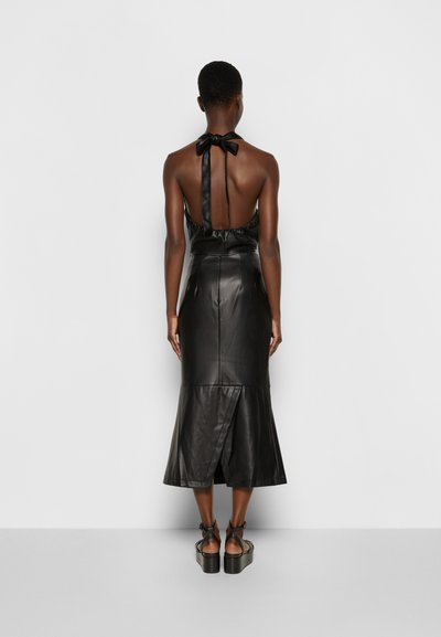 Vestido de couro preto com decote halter e costas nuas, apresentando uma cintura ajustada e bainha godê. O design inclui um detalhe de laço no pescoço.