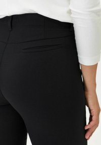 Pantaloni neri realizzati in tessuto liscia con un design aderente. Presentano una tasca posteriore con un discreto dettaglio di cucitura.