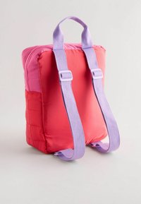 Kompakt ryggsäck i rosa och röd, med en vadderad design. Inkluderar lila remmar och handtag, med en slät och glansig yta.