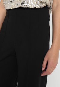 Svarta byxor med hög midja och slät tyg, parat med en paljett-topp som visar en skimrande, texturerad design.