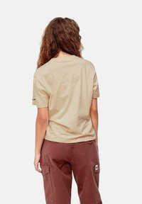 Camiseta de algodón beige de manga corta, con cuello redondo, corte relajado y detalle del logo en la manga izquierda, combinada con pantalones cargo marrones.