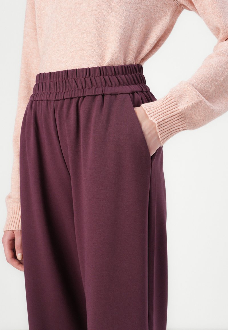 Paarse broek met elastische tailleband en zijzakken, gemaakt van zachte stof. Gemaakt in combinatie met een lichtroze, geribbelde top met lange mouwen.