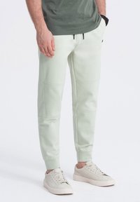 Lichtgroene sweatpants met een taps toelopende pasvorm, voorzien van zijnaad en geribde boorden, gecombineerd met beige sneakers. Glad, zacht textuur van de stof.