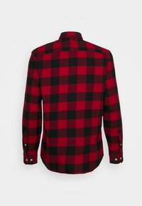 Camicia a maniche lunghe a scacchi rossi e neri con polsini abbottonati, mostrata da dietro su uno sfondo bianco.