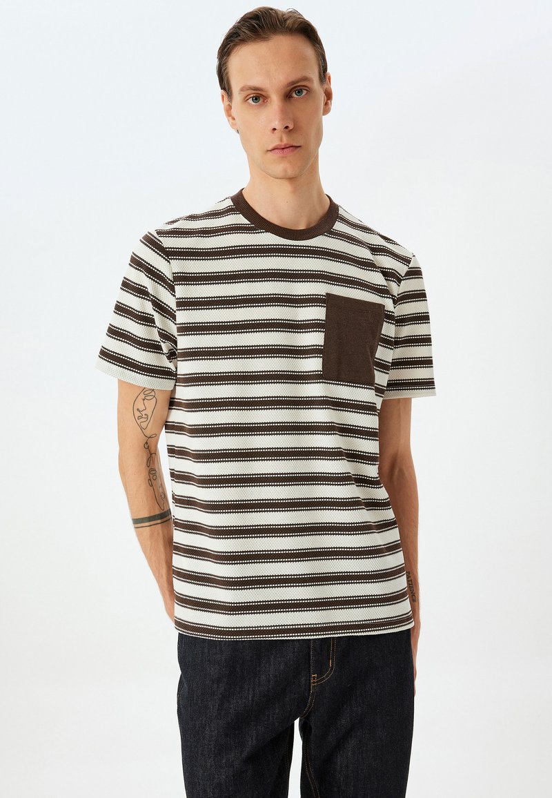 Stribet t-shirt i beige og brun bomuld. Ribbet rund hals, korte ærmer, med en brun brystlomme, struktureret stof.