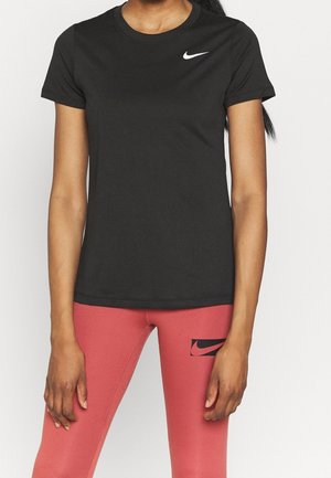 Vrouw draagt een zwart Nike T-shirt met korte mouwen en hoog getailleerde roze leggings met een zwart Nike-logo op de dij.