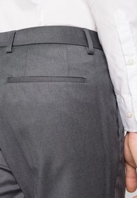 Gray trousers with a smooth texture, slim fit design, and a back pocket sans flap. Paired with a white collared shirt.