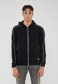 Felpa con zip nera con strisce bianche sui maniche, polsini a costine e cappuccio, realizzata in morbido cotone.