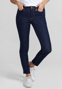 Jeans skinny azul oscuro con una cintura alta, que cuentan con un cierre de botón y cremallera, bolsillos delanteros y traseros, y detalles de costura en contraste.