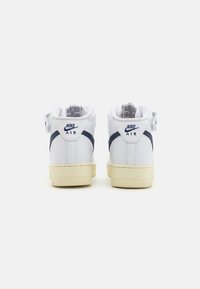 Hvite høye sneakers med marineblå detaljer, teksturert lær, polstret krage og gummisåle. Har "Nike Air" merking på baksiden.