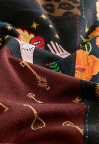 Farebné tkanivo so vzormi kľúčov, kvetov a štýlizovaných rúk. Základná farba je čierna s burgundskými akcentmi a zložitými detailmi.