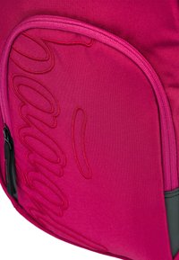 Zaino in tessuto rosa con logo ricamato in rilievo. Presenta una tasca laterale con zip e una texture liscia e resistente. Accenti neri a contrasto.