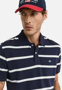 Polo di colore blu navy con strisce orizzontali bianche, maniche corte e colletto. Presenta un piccolo logo ricamato sul petto.