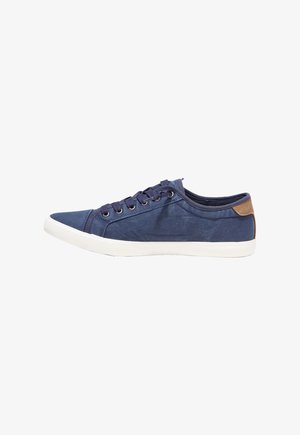 Sneaker bassa in tela blu navy con suola bianca, lacci blu navy, occhielli metallici e toppa marrone sul tallone su sfondo uniforme.