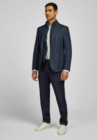 Marineblauer kariertes Sakko mit hohem Kragen, kombiniert mit dunklen Jeans und weißen Sneakers. Strukturiertes Gewebe und taillierte Passform.