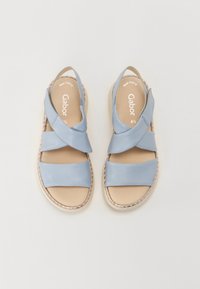 Sandales en cuir bleu avec des lanières croisées, semelles intérieures beiges et un bord tissé. Elles présentent une semelle plate et un design simple, étiquetées "Gabor."