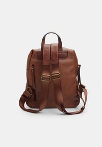 Zaino in pelle marrone con spalline regolabili, tasca con zip e accessori in tonalità oro. Presenta una superficie testurizzata e una forma rettangolare.