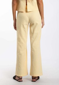 Pantalones de cuadros amarillos con una tela texturizada, con un corte de pierna ancha y dobladillos rematados, combinados con sandalias negras con tiras.