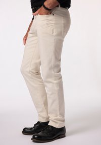 Pantalones beige ajustados con una textura suave, que cuentan con bolsillos frontales y mínimos detalles de costura, combinados con zapatos negros.