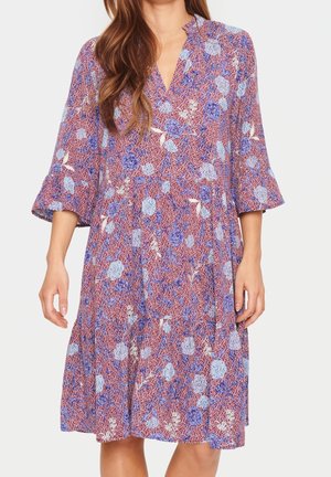 Kniejurk met paarse en blauwe bloemenprint, V-hals en 3/4 klokmouwen, gedragen door een persoon met lang bruin haar.