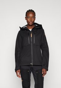 Veste noire imperméable avec une fermeture éclair sur le devant, une capuche ajustable et deux poches poitrine. Affiche une texture lisse et un branding discret.
