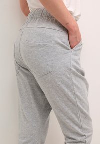 Grå sweatpants lavet af blødt stof, med elastisk talje, sidelommer og en glat, let tekstureret overflade.