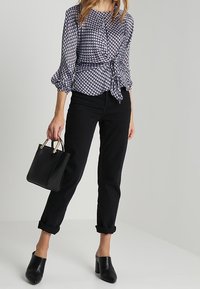 Marinblus med vitt mönster och puffärmar, knuten i midjan; kombinerad med svarta uppvikta jeans och svarta klackskor.