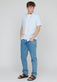 Lichtblauwe shirt met korte mouwen over een witte T-shirt, gecombineerd met lichtblauwe jeans en zwarte sandalen. Eenvoudig ontwerp en casual pasvorm.