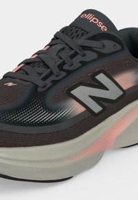 Κοντινό πλάνο σε μαύρο και ροζ Running παπούτσι New Balance με γκρι σόλα και λογότυπο "N" στο πλάι, που δείχνει κορδόνια και λεπτομέρειες από πλέγμα στην επάνω όψη.