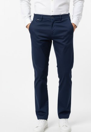 Pantalones azul marino de corte ajustado con textura suave, que cuentan con cierre frontal de cremallera, botón y bolsillos laterales. Combinados con zapatillas blancas.