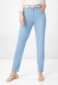 Lysblå denim jeans med lige ben, forlommer og et beige bælte. Kombineret med nude flip-flops, præsenteret mod en neutral baggrund.
