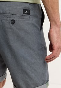 Shorts grigi in tessuto testurizzato con motivo a spina di pesce, dotati di chiusura con bottone e un'etichetta nera con logo sulla tasca posteriore.