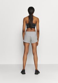 Harmaat urheilushortsit, joissa on vyötärö, yhdistettynä mustaraidalliseen toppiin. Yksinkertainen muotoilu ja pehmeä kangas. Takakenkä.