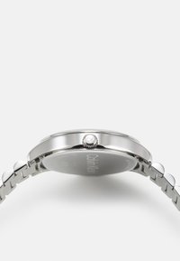 Reloj de pulsera plateado con caja redonda, correa de acero inoxidable y corona de pulsar y arrastrar. La parte posterior está marcada con el nombre de la marca "Calvin Klein."