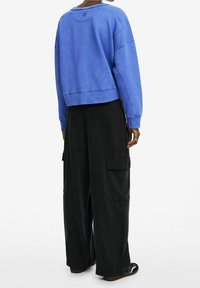 Felpa blu corta con scollo rotondo e orlo a coste, abbinata a pantaloni cargo neri a gamba larga con tasche laterali.