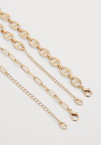 Catena in metallo dorato, composta da tre segmenti: grandi ovali collegati, disegni più piccoli intrecciati e una chain sottile con un gancio a granchio.