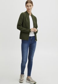 Vihreä kerekkokardigan, jossa on korkea kaulus, päällä valkoinen paita. Yhdistetty sinisiin slim fit -farkkuihin ja vaaleanharmaisiin lenkkareihin.