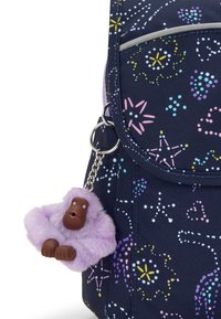 Lila fluffig gorillanyckelring fäst vid en marinblå ryggsäck med färgglada stjärnor och hjärtan mönster.