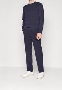 Granatowy sweter i dopasowane spodnie wykonane z miękkiego materiału; mają okrągły dekolt i subtelne logo na piersi; zestawione z białymi sneakersami.