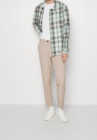 Camicia di flanella a quadri azzurro chiaro e nero sopra una t-shirt bianca, abbinata a pantaloni beige e sneakers bianche. Design semplice, vestibilità comoda.