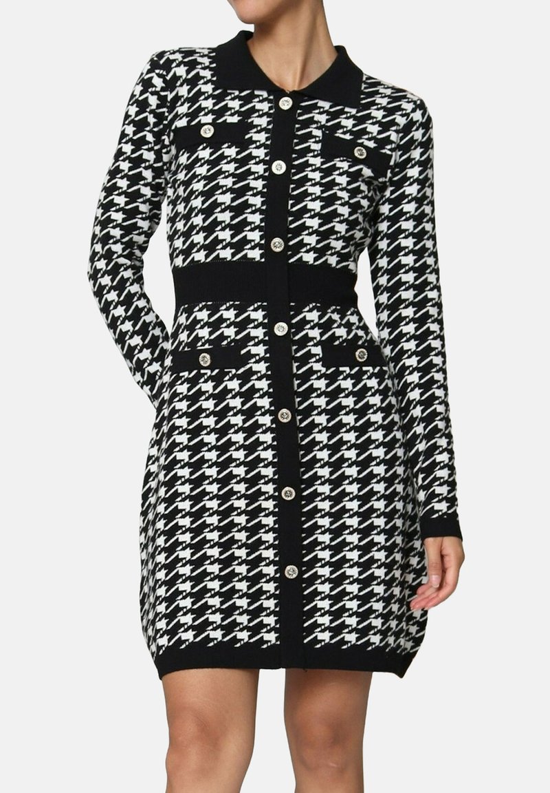 Femme portant une robe boutonnée à manches longues avec un motif pied-de-poule noir et blanc, un col et des détails de poches.